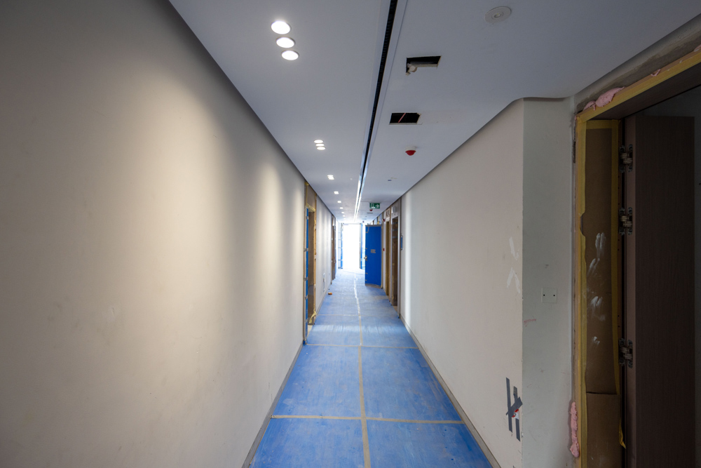 Beach Walk Residence A corridor under construction, featuring blue flooring, several doors, and bright ceiling lights.
